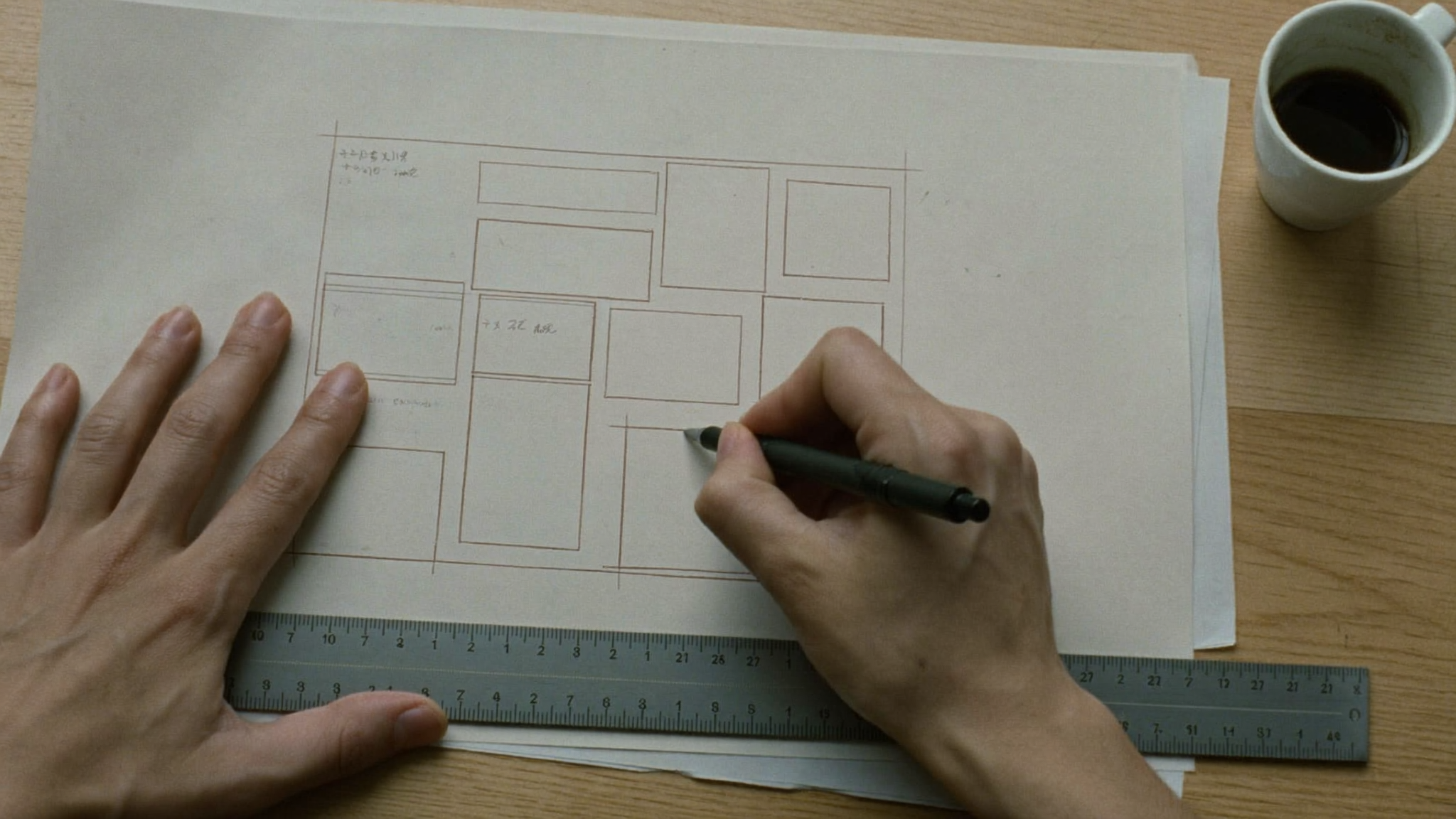 Hands ruling a layout grid onto tracing paper with a fine pen