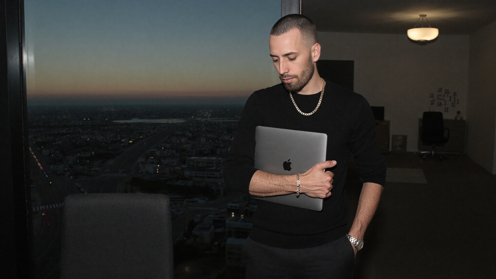 A founder working alone with a laptop beside a window at dusk