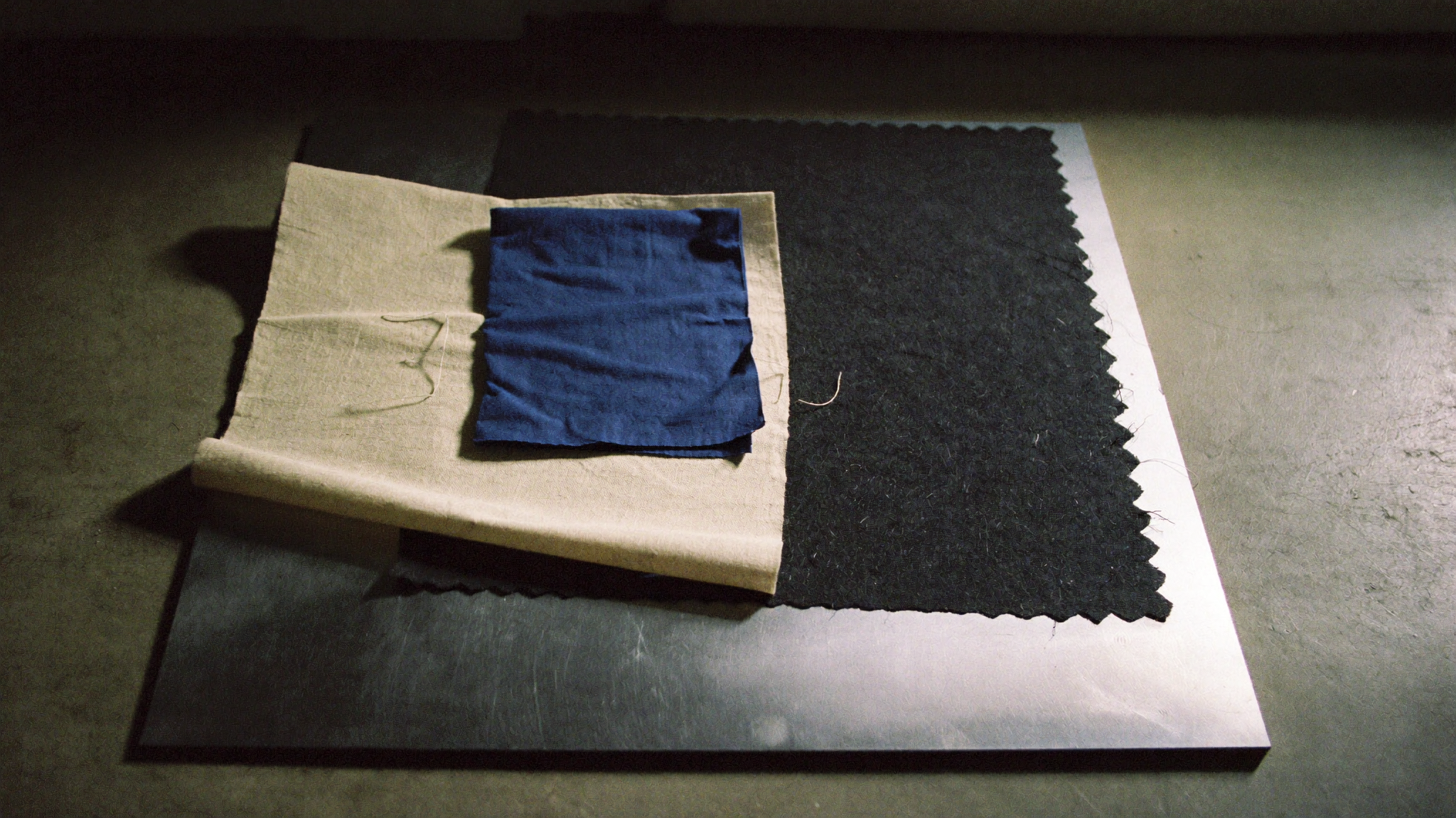 Folded fabric and material swatches in black, charcoal and off-white with one deep blue accent