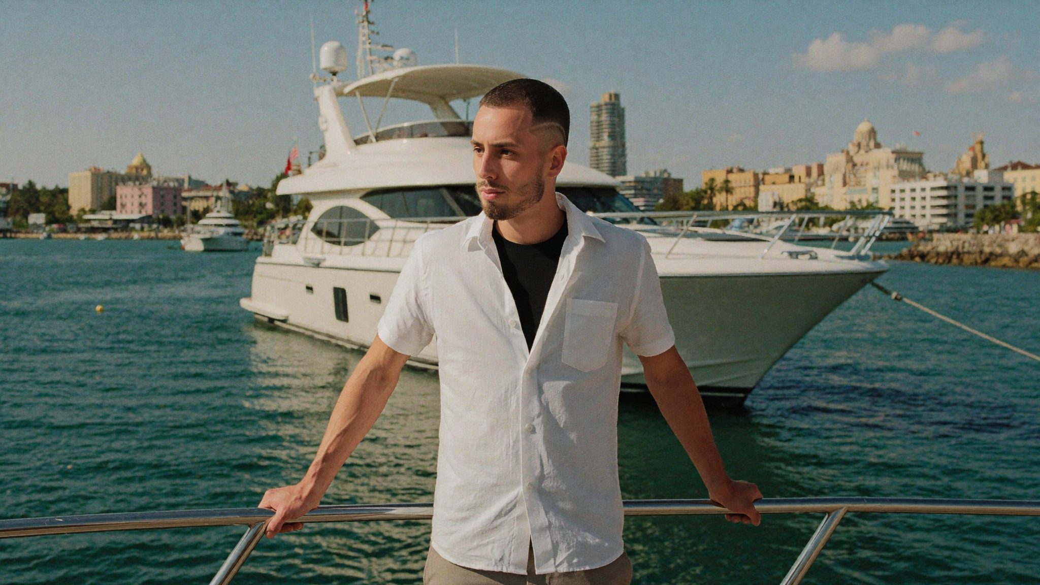 Founder in an open linen shirt at the stern rail of a motor yacht off Miami at golden hour