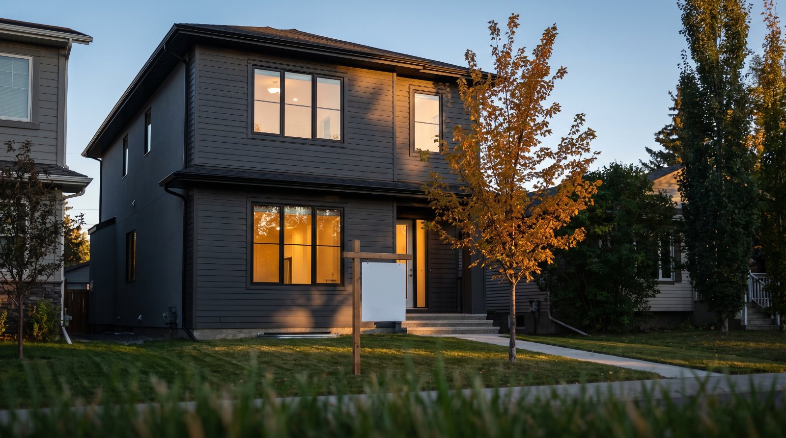 A modern Canadian infill home at dusk with a blank sign on the front lawn