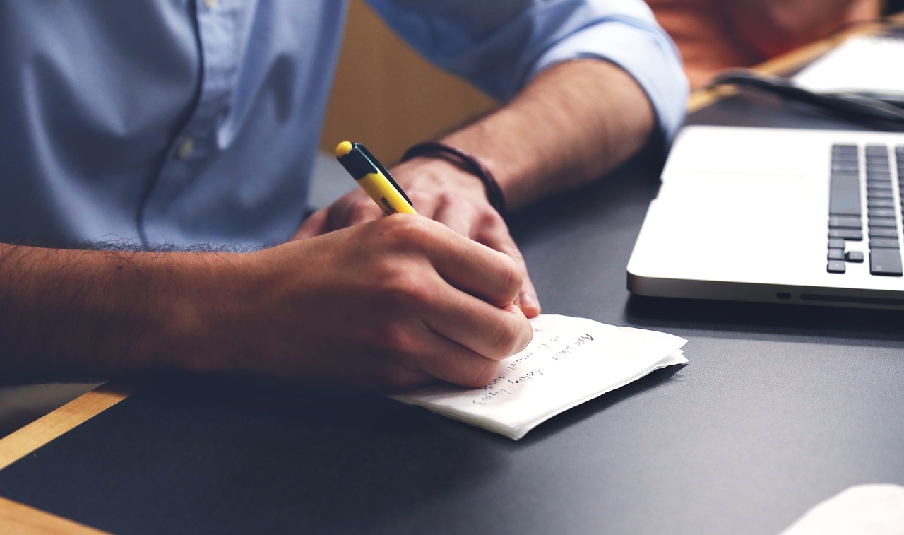 Writing notes in a notebook beside a laptop, illustrating the written chatbot governance record a business keeps.