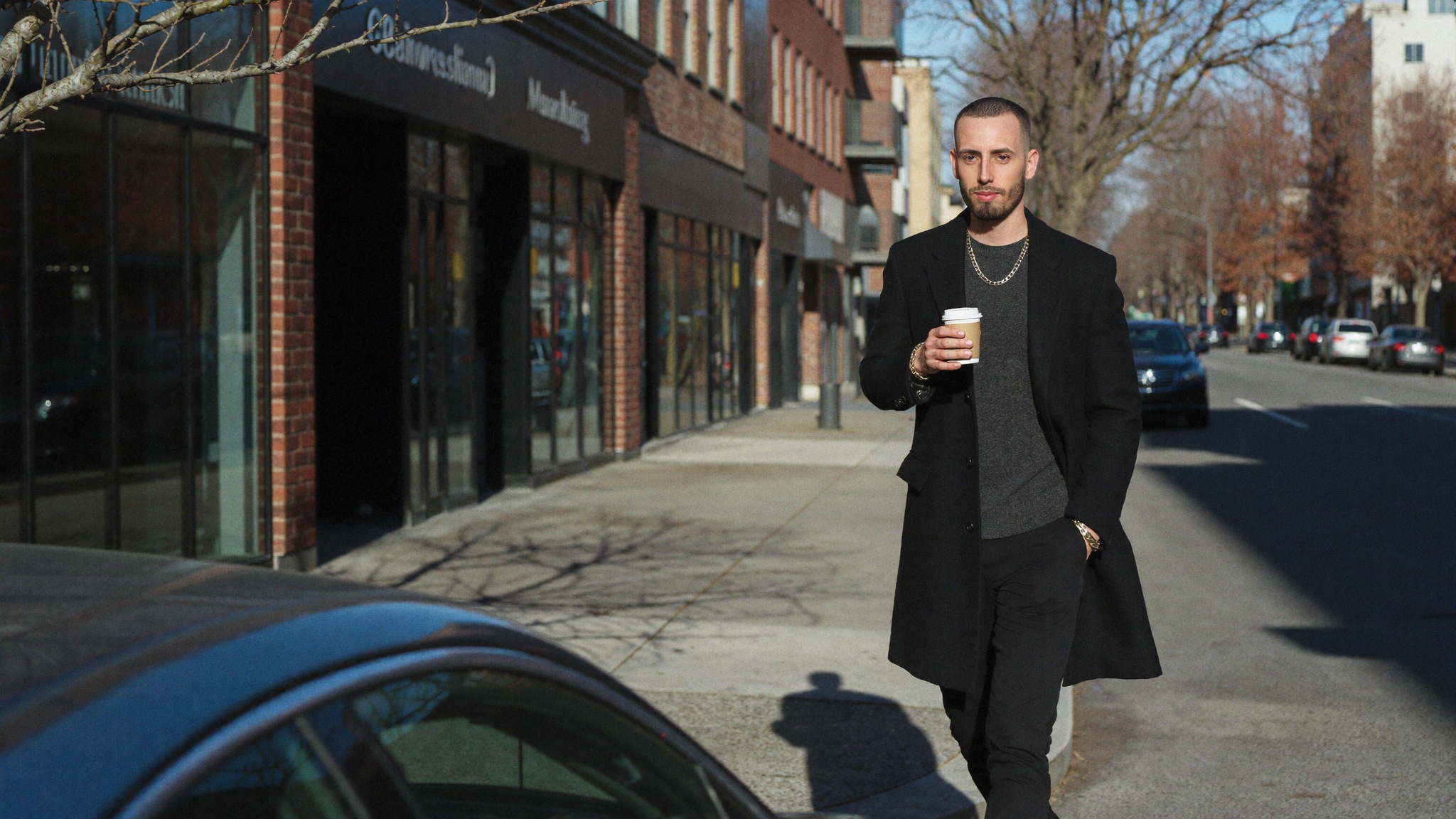A man in a black overcoat walks past a row of independent storefronts on a Canadian main street, the kind of local business whose bookings depend on its Google review profile.