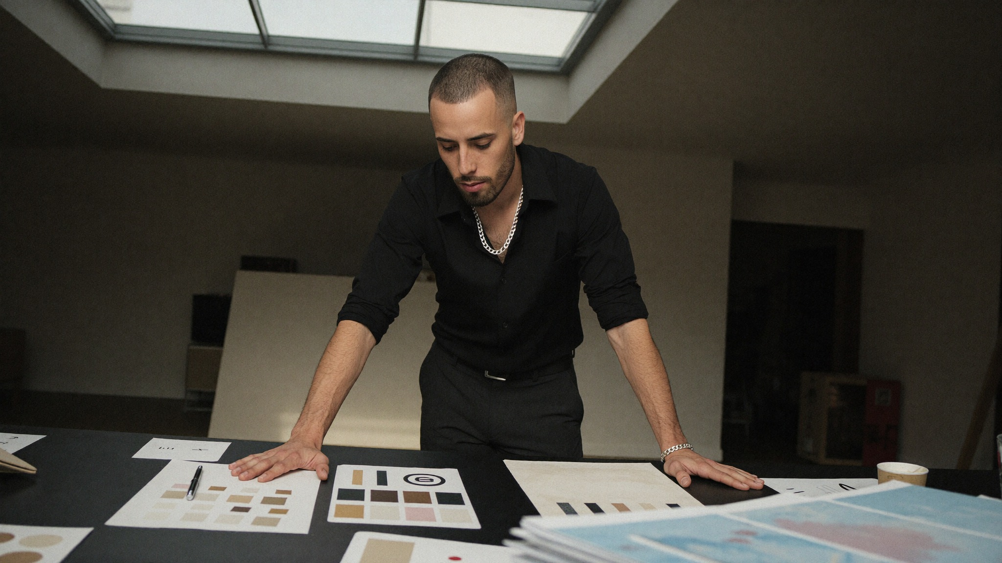 Cody Wise reviewing printed brand identity boards, colour chips and logo sheets on a studio table.