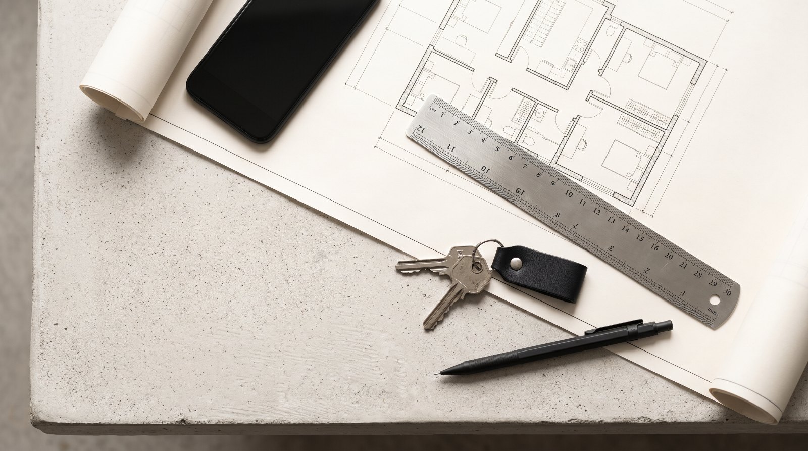 A floor plan, a steel scale ruler and a set of house keys on a concrete table