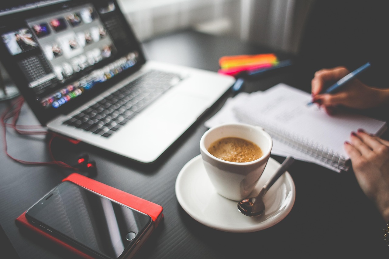 A laptop, notebook and coffee on a desk, representing separate local pack and AI visibility workstreams planned side by side.
