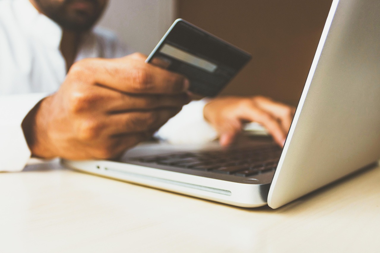 Hands at a laptop holding a payment card, illustrating where mandatory fees appear during an online checkout.